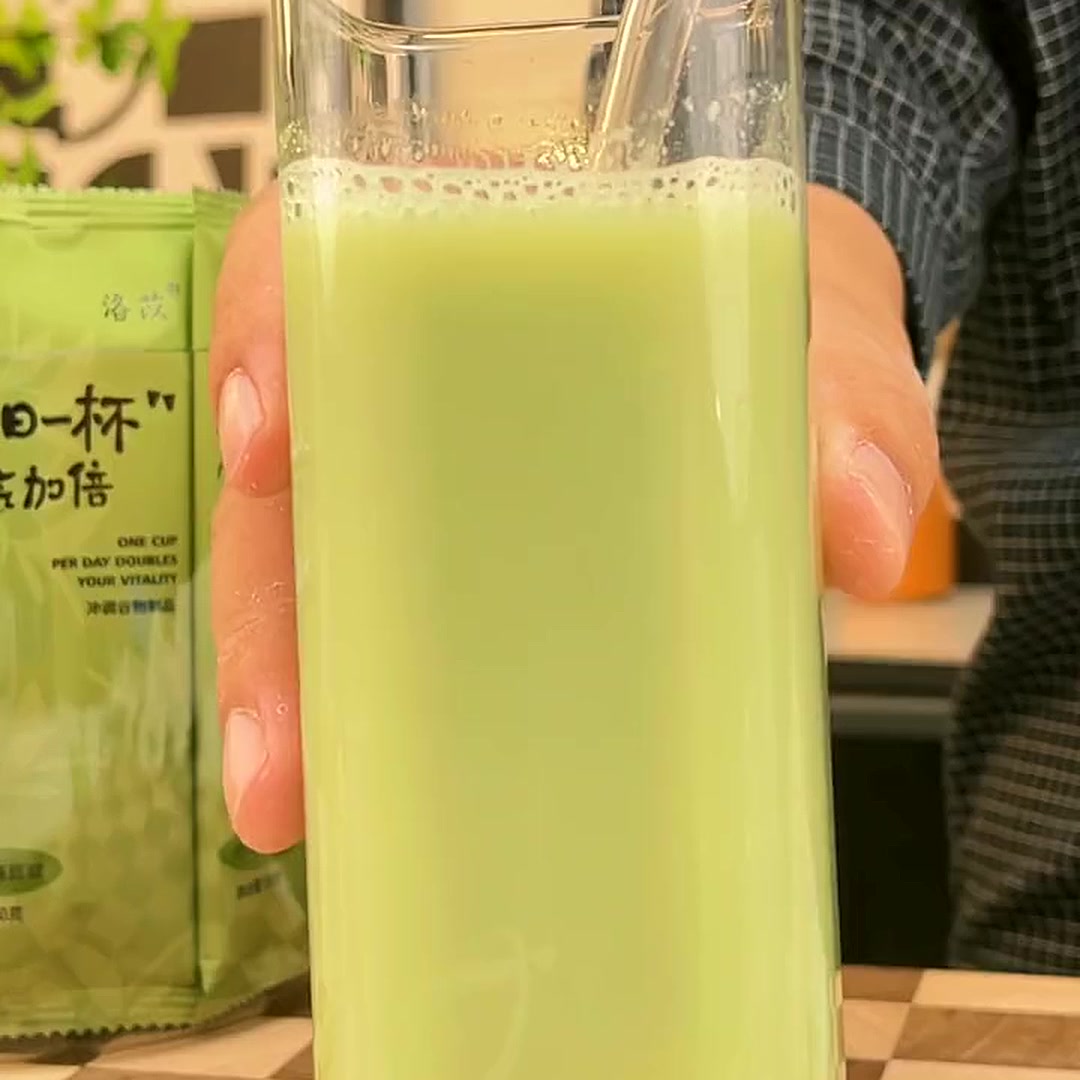 冲泡成杯特写：手持玻璃杯绿色豆浆 + 水瓜吸管，背景洛苡条装产品